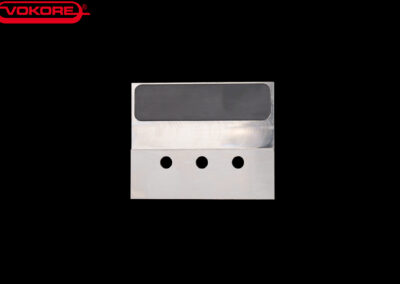 Rechteckiges Metallmesser mit drei Bohrungen, dargestellt vor schwarzem Hintergrund