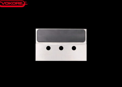 Rechteckiges Metallmesser mit drei Bohrungen, dargestellt vor schwarzem Hintergrund