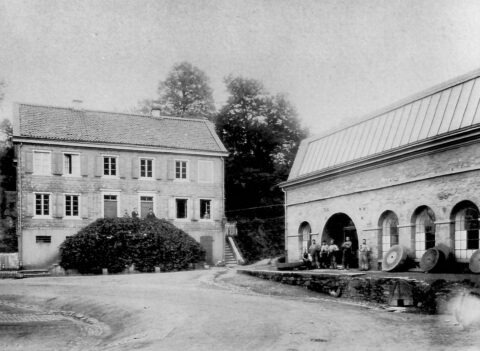 Historische Schwarz-Weiß-Aufnahme eines Fabrikgebäudes mit Arbeitern vor dem Eingang